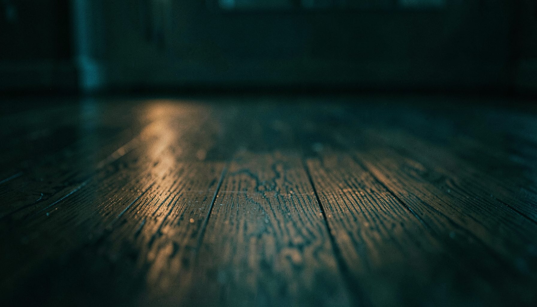 Water spreading across a hardwood floor in a dimly lit room, reflecting soft amber light with deep shadows and a somber mood